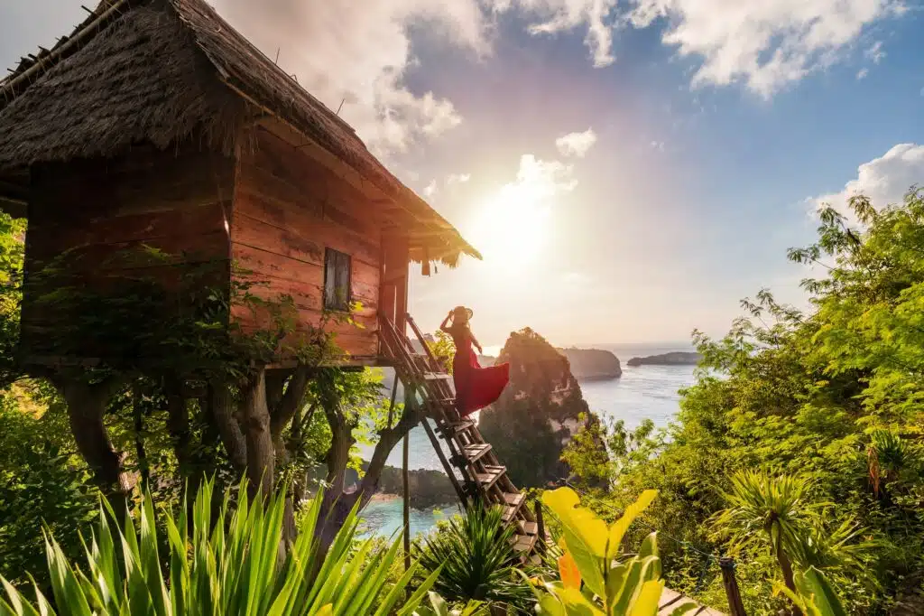 Action im Urlaub: Junge Frau Reisende genießen und suchen schönen Sonnenaufgang am Baumhaus